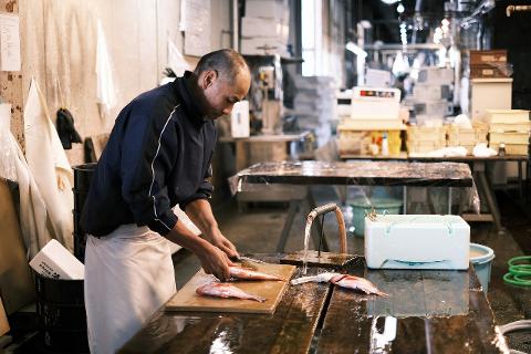 Japan Kanazawa Seafood Auction & Fine Dining Tour – 1-Day Trip A man in an apron prepares fish on a wooden cutting board in a bustling market.