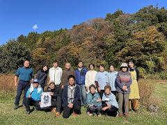 Explore the Local Morning Charm of Shiobara Onsen with a Satoyama Mini-Trek and Local Breakfast Delight A group of people poses for a photo in front of a wooded hillside with fall foliage.