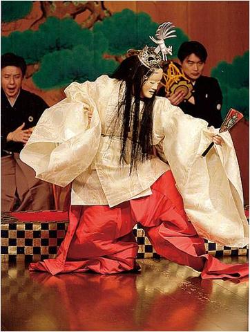 一位身着歌舞伎服装、戴着面具和王冠的演员在舞台上手持扇子，由两位身着传统服饰的乐师伴奏。