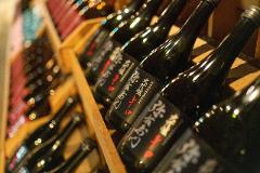 A close-up shot of dark sake bottles with white and red labels arranged in a wooden crate at a historic sake brewery.
