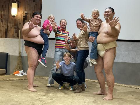 A sumo wrestler holds a child as a group poses for a photo in front of a sumo ring.
