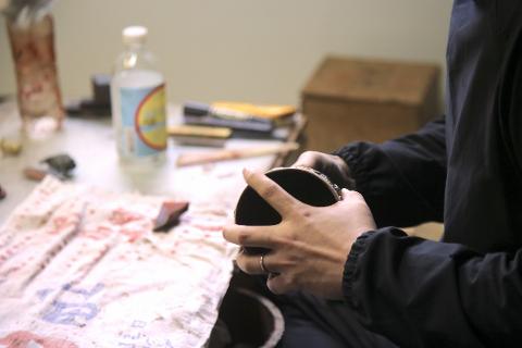 Wajima Full-Day Lacquer & Nature Tour – Ishikawa Craft Walk A person's hands hold a lacquered bowl over a patterned cloth, surrounded by crafting tools and supplies.