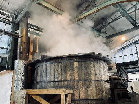 Nagano Day Tour: Agar Factory & Tasting in Chino Highlands A large wooden vat, emitting steam, is situated in an industrial setting with exposed metal beams and corrugated walls.