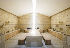 Ishikawa 90-Minute Gold Leaf Pottery Experience with Tea Ceremony A sunlit, minimalist studio with stone walls and wooden furniture features shelves displaying various pottery pieces.