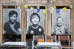 "Reborn-Art" Tour: Experience Contemporary Art on the Oshika Peninsula Portraits of three Asian women are displayed on a wooden door, with flags indicating the "Reborn-Art Festival 2017" hanging above them.