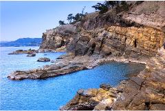 The image captures a serene coastal landscape with layered cliffs meeting the bright blue ocean, dotted with rocky outcrops.