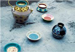 Nationally Treasured Technique - Kinsai Pottery Studio Tour A collection of intricately decorated ceramic vessels, including a teapot and several small bowls, rests on a textured gray surface.