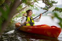 Visit the Spring Water Flowing into Lake Shirakaba and Experience the Origins of Our Connection with Nature – Private Guided Canoe Tour A woman in a yellow life vest paddles a red kayak on a serene lake, with two other kayakers behind her.