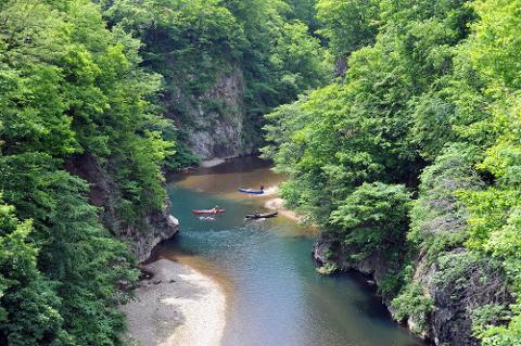 A scenic view of a river with lush green trees on both sides, and three canoes with people enjoying the water.