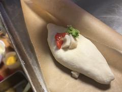 A close-up shows an uncooked piroshki on parchment paper with toppings like red pepper, fish slices, and green garnish.