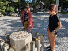 Two women admire a stone monument covered in coins in a courtyard at Ise Grand Shrine, Japan.