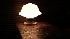 Visit Nikko's Craftsmanship Workshop to Experience Historic Techniques A lit lamp with a decorative lampshade sits on a table with intricate wood carvings, set against a dark, textured background.