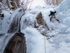 An ice climber ascends a frozen waterfall in Nikko, Japan, surrounded by icicles and snow-covered rocks.