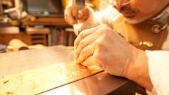 A Buddhist altar metalwork master uses a hammer and chisel to engrave intricate floral patterns onto a piece of copper.