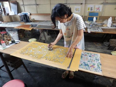 A woman in an apron dyes a scarf in a workshop.