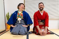 Two people in traditional Japanese attire laugh while kneeling on a tatami mat.