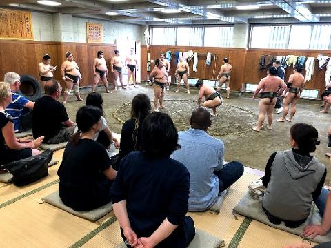 A group of spectators watches sumo wrestlers practice in a dojo.
