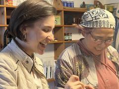 Two women, one in a quilted jacket and the other with a headscarf, joyfully make piroshki in Hakodate.