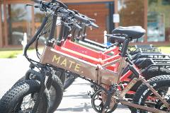 A row of colorful MATE electric bikes are parked outside on a sunny day.