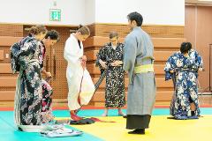 Päť ľudí je v miestnosti s drevenými stenami a viacfarebnou podlahou a obliekajú si japonské rúcha.
