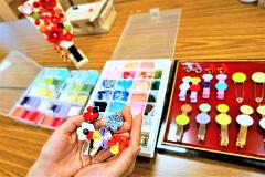 Traditional Japanese Craft Experience -- "Tsumami-Zaiku" Accessory Hands hold colorful fabric flowers attached to hair clips and a safety pin, with various craft supplies visible in the background.