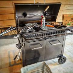 A charcoal grill with tools, a gas cylinder, and a box on top is set up outdoors.