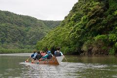 A group of people are paddling a traditional Sabani boat on the Nakaragawa River, surrounded by lush green forests and hills.