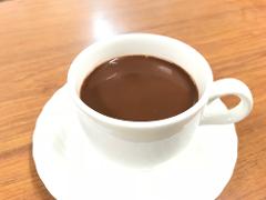 A white cup of hot chocolate sits on a white saucer on a wooden surface.