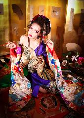 Eine schöne asiatische Frau in einem traditionellen Kimono und aufwendigem Haarschmuck sitzt vor einem goldenen Paravent mit Blumen und Kalligrafie.