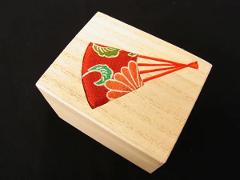 A wooden box with an inlaid fan design made of colorful fabric and red thread on a black background.