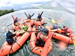 A group of friends enjoy a scenic rafting tour on Lake Chuzenji, posing for a selfie with a mountain in the background.