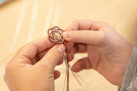 Nagano Day Trip: Traditional Washi & Mizuhiki Workshop Hands carefully tie a traditional Japanese mizuhiki knot made of thin paper cords.