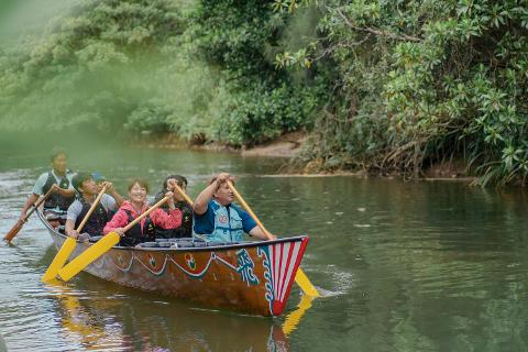 A group of people are paddling a traditional Sabani boat on the Nakaragawa River, surrounded by lush green vegetation.
