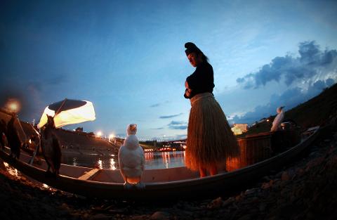 A man in traditional attire stands on a boat with cormorants at dusk.