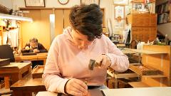 A person wearing a pink hoodie hammers on a metal object in a workshop.