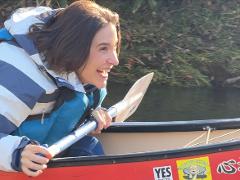 Une femme pagaie dans un canoë sur la rivière Shiodomari et sourit avec enthousiasme.
