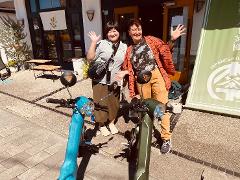 Two women pose with rental electric bikes outside a shop in Ise, Japan.