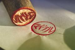 A close-up shot of a traditional Japanese hanko seal made of natural wood, stamped in red ink on a piece of paper.