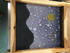 A framed piece of dark blue handmade paper features a dark silhouette on the left and a yellow, orange, and white abstract pattern on the right, with gold flakes scattered throughout.