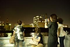 Three women are observing and photographing industrial buildings at night.