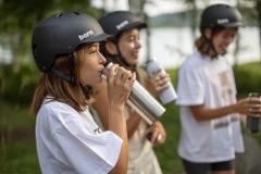 Three women wearing helmets and casual clothing drink from water bottles while on a break during an e-bike tour.