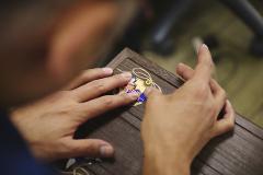 A close-up shot captures a person's hands carefully working on a piece of intricate kiribako woodwork, highlighting the delicate artistry involved.