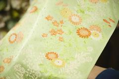A light green fabric is beautifully adorned with a delicate floral pattern in shades of orange and yellow, hinting at intricate artistry.
