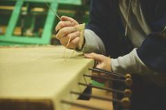 A craftsman skillfully stitches a mini tatami mat with a needle and yellow thread.