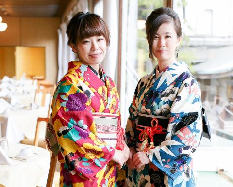 Due donne giapponesi, una accanto all&#39;altra, indossano colorati kimono e sorridono alla telecamera in quella che sembra essere la cornice di un ristorante.