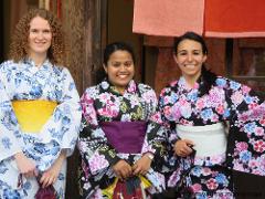 Three women in traditional Japanese kimonos smile for a photo in front of a doorway.