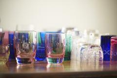 A collection of colorful, etched glass tumblers and cups are displayed on a wooden surface.