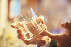 A hand holds a clear glass with etched designs while another finger points to it, suggesting a demonstration or inspection.
