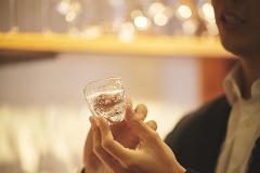 A person holds a small, intricately patterned glass filled with a clear liquid.