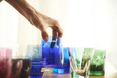 A hand picks up a blue glass decorated with small fish among other colorful glasses.